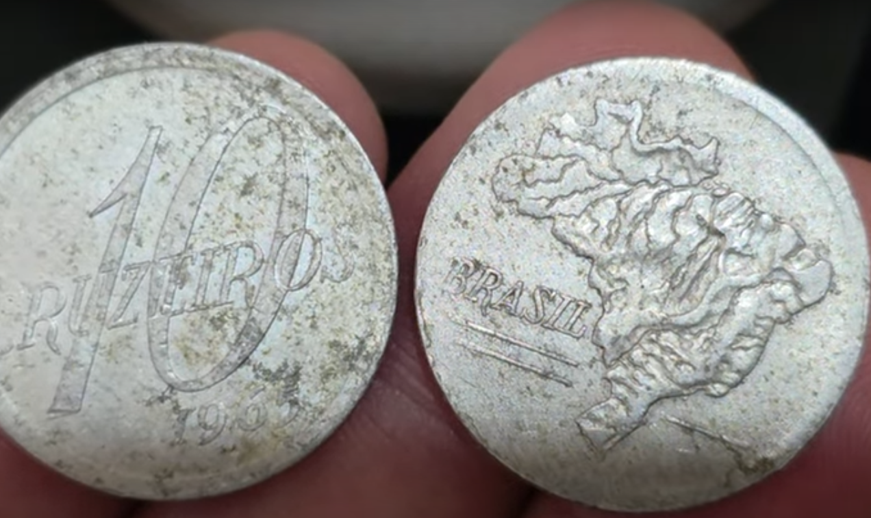 Moedas antigas de 10 Cruzeiros sendo comparadas, uma de 1964 e outra de 1965.