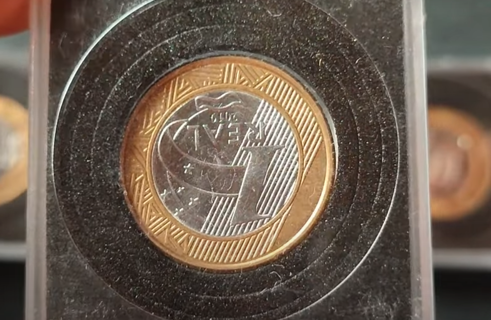 Moeda de 1 real com reverso invertido dentro de proteção circular preta