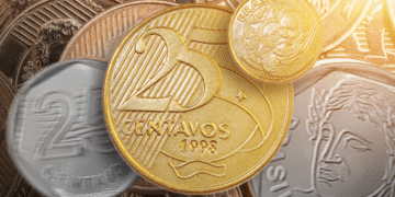 Moeda brasileira de 25 centavos de 1998 em destaque, rodeada por outras moedas comuns.