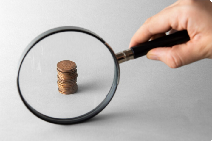Imagem mostrando uma pilha de moedas observada através de uma lupa, simbolizando a detecção de falsificações em moedas e cédulas.